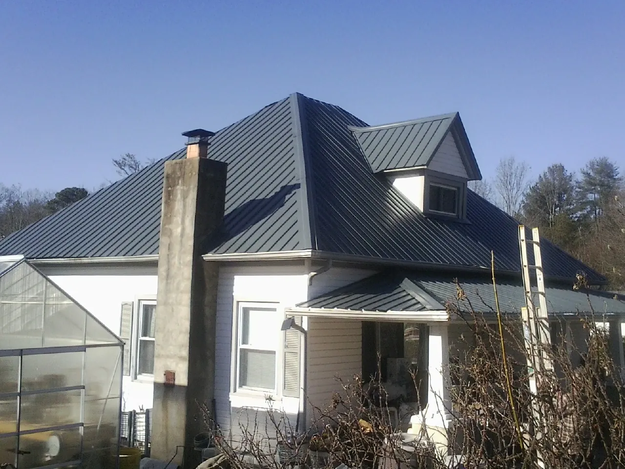 Dark blue standing seam metal roof on a white farmhouse with dormer — Slate & Tile Roof Repair by Roofing Brothers in Shedd