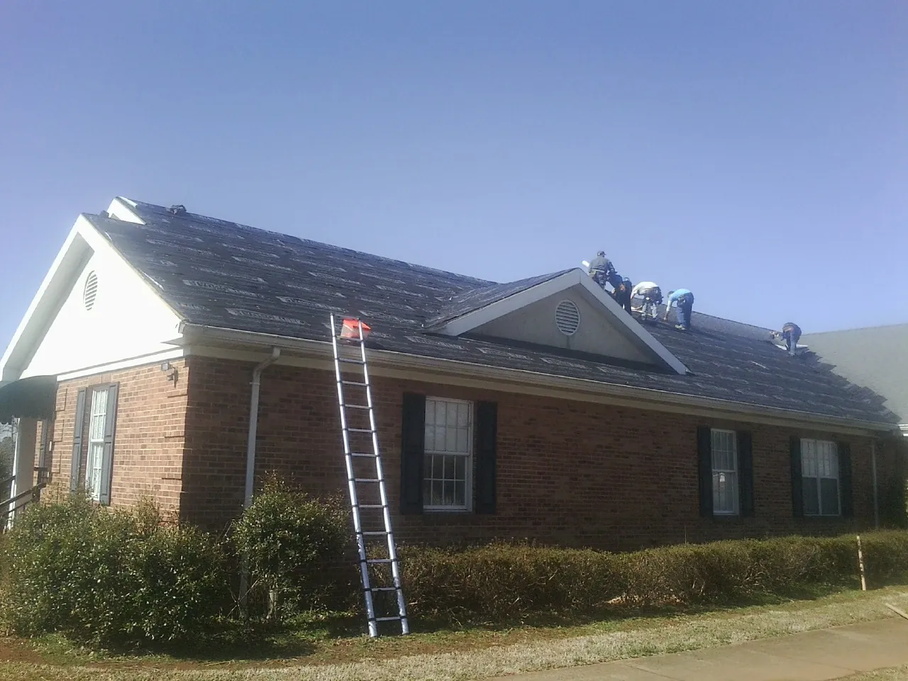 Crew tearing shingles off a brick ranch roof with a ladder set — Emergency Roof Repair work by our crew in Shedd