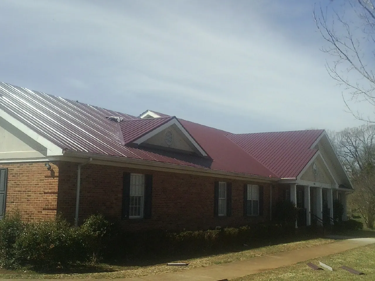 Red metal roof with gabled entries on a long brick building, from a Hail Damage Roof Repair job in Shedd
