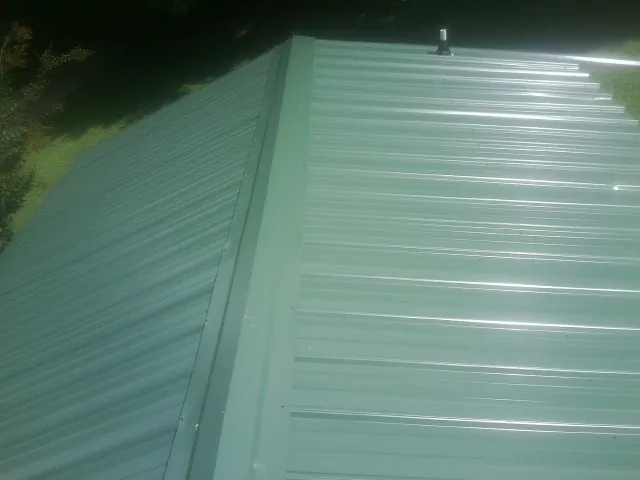 New green metal panels meeting at the ridge of a roof — Flat Roof Repair work by our crew in Shedd