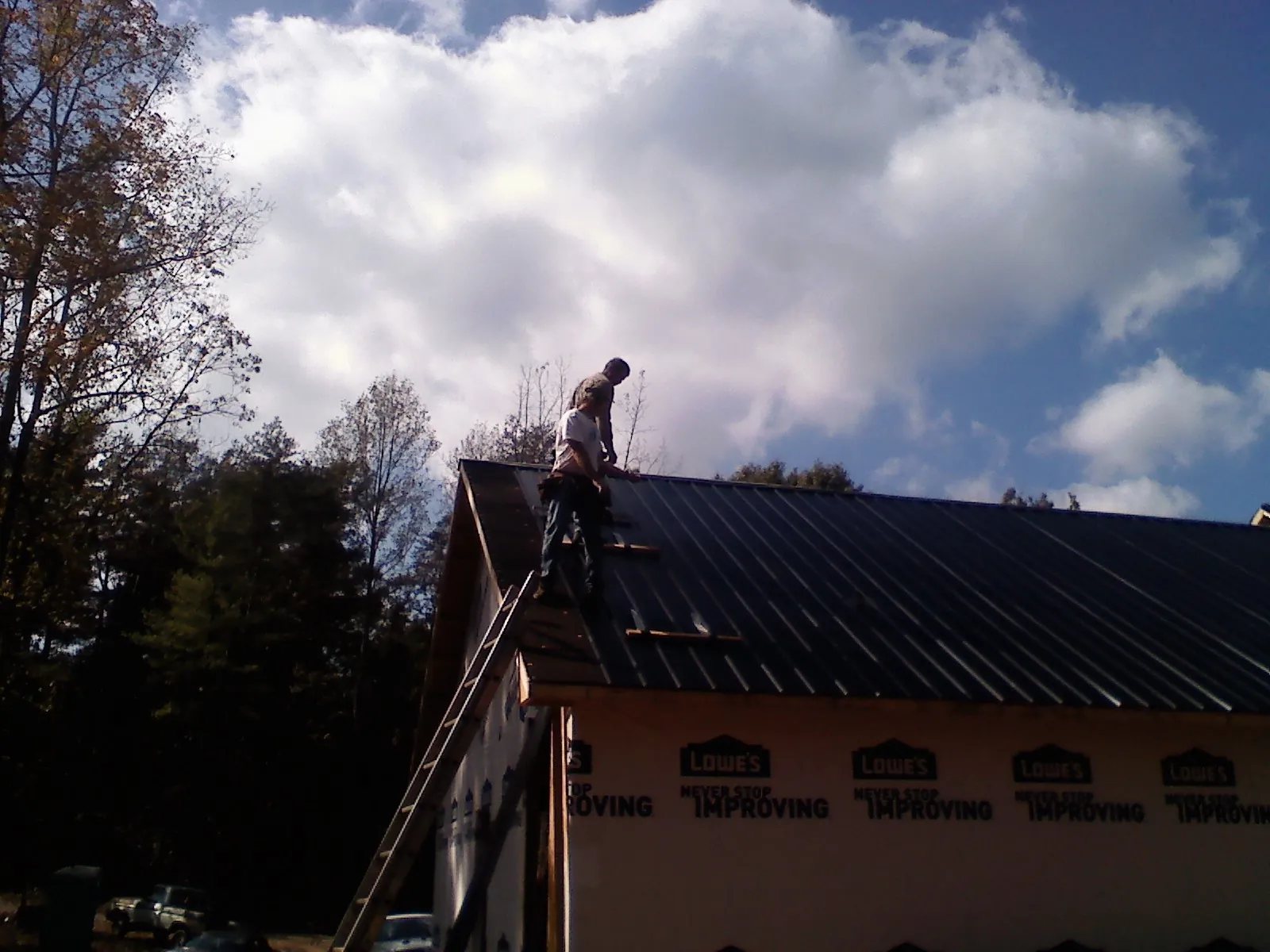 Roofer fastening dark metal panels high against a cloudy sky, from a Roof Inspection job in Shedd