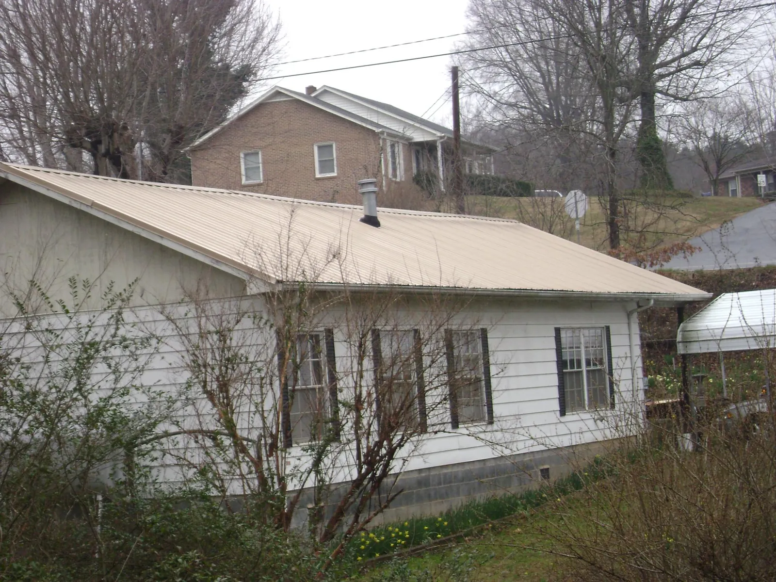 Tan metal roof on a white sided house set into a hillside — Commercial Roofing by Roofing Brothers in Shedd